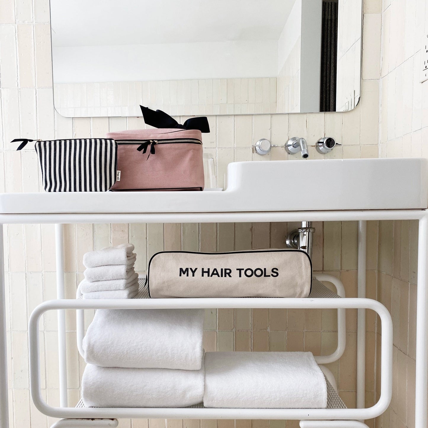 Bag-all Roomy Hair Wrap Tools Travel Case in cream, displayed on bathroom shelf with white towels and pink toiletry bag, showcasing organized storage for hair styling tools.