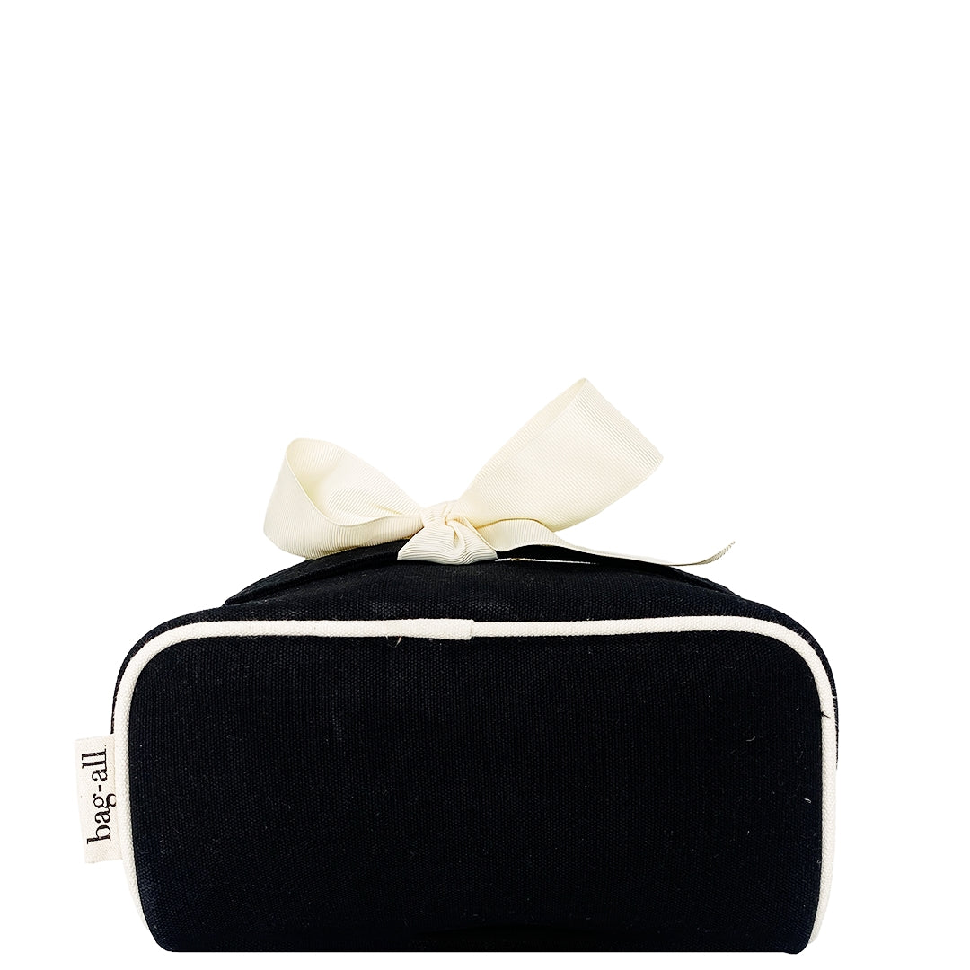 Bottom view of Bag-all Accordion Box Makeup & Toiletry in Black. Features durable cotton fabric, contrast piping, and a chic bow detail