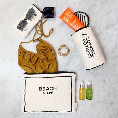 Bag-all Stylish Beach Essentials 3-pack in cream featuring waterproof pouch, sunglasses case, and toiletry bag displayed with beach accessories including sunscreen, sunglasses, and beauty oils on marble surface