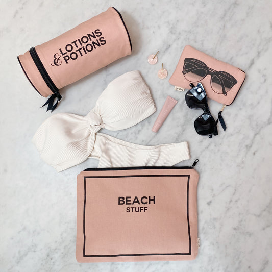 Bag-all Stylish Beach Essentials 3-pack in pink featuring waterproof beach stuff pouch, lotions and potions case, and sunglasses holder with black trim and monogram option, laid on marble surface