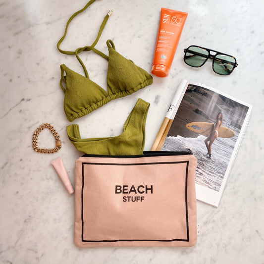 Bag-all Monogram Beach Pouch in pink with waterproof lining, displayed with olive green bikini, sunscreen, sunglasses and beach photo, perfect for organizing beach essentials