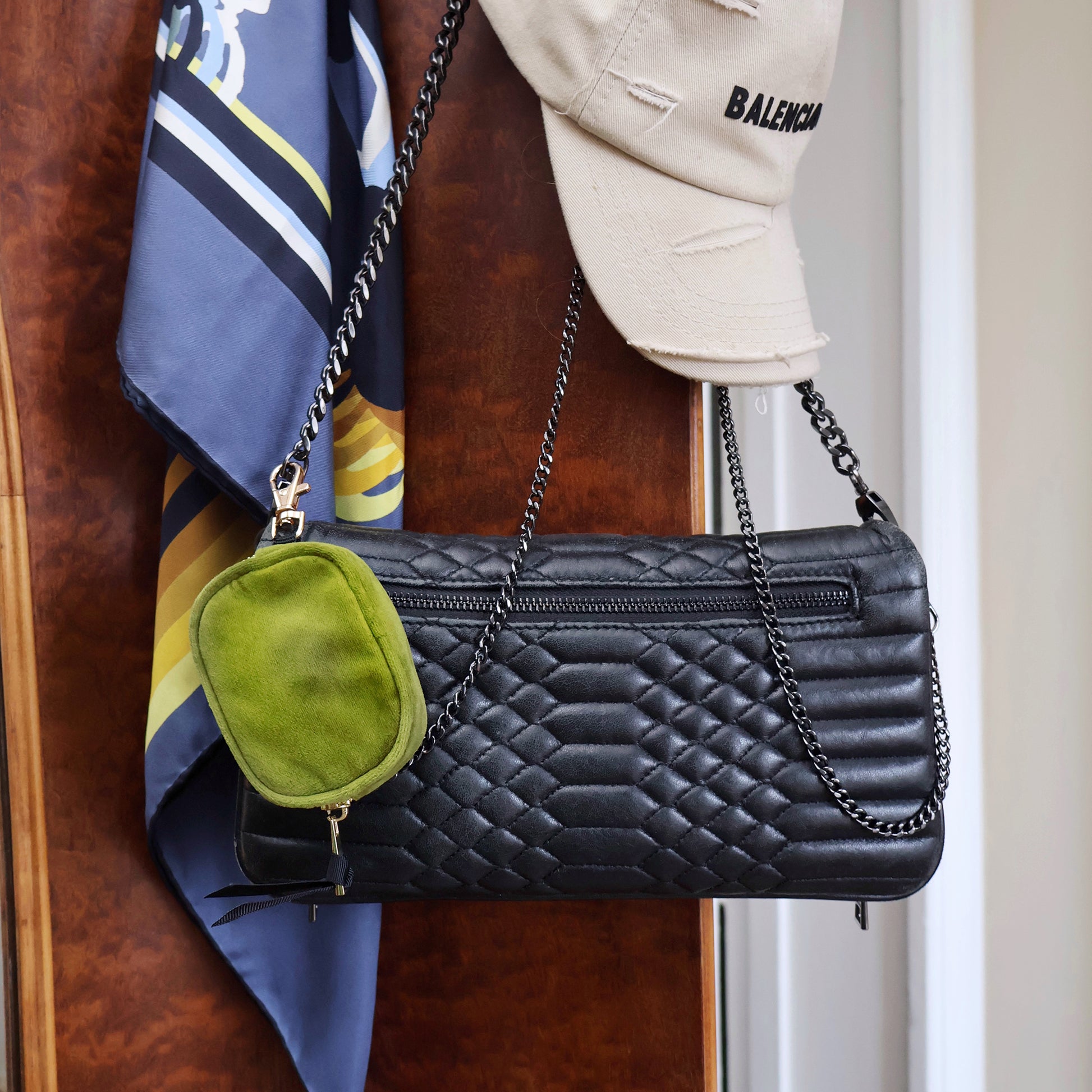 Bag-all green velvet Earbuds Case with gold clasp shown attached to black quilted handbag, featuring protective eco-friendly design for AirPods and earbuds, perfect for everyday organization and style.