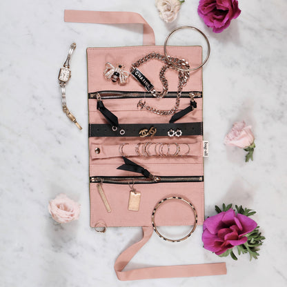 Bag-all Couture Jewelry Roll in Medium Pink Velvet, featuring multiple compartments with zippers, displaying organized jewelry including necklaces, rings, and bracelets on a marble surface with pink and purple roses