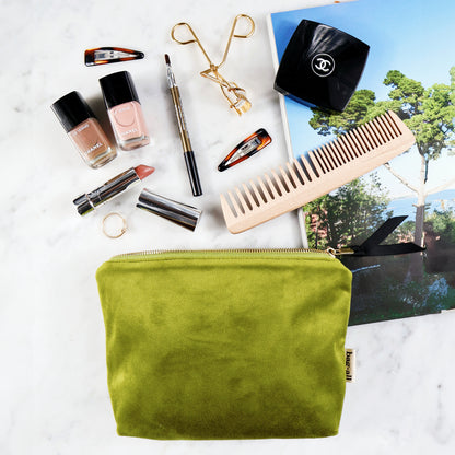 Bag-all My Makeup Pouch in luxurious green velvet with waterproof coated lining, displayed with premium beauty essentials including nail polish, lipstick, eyelash curler and wooden comb on marble surface