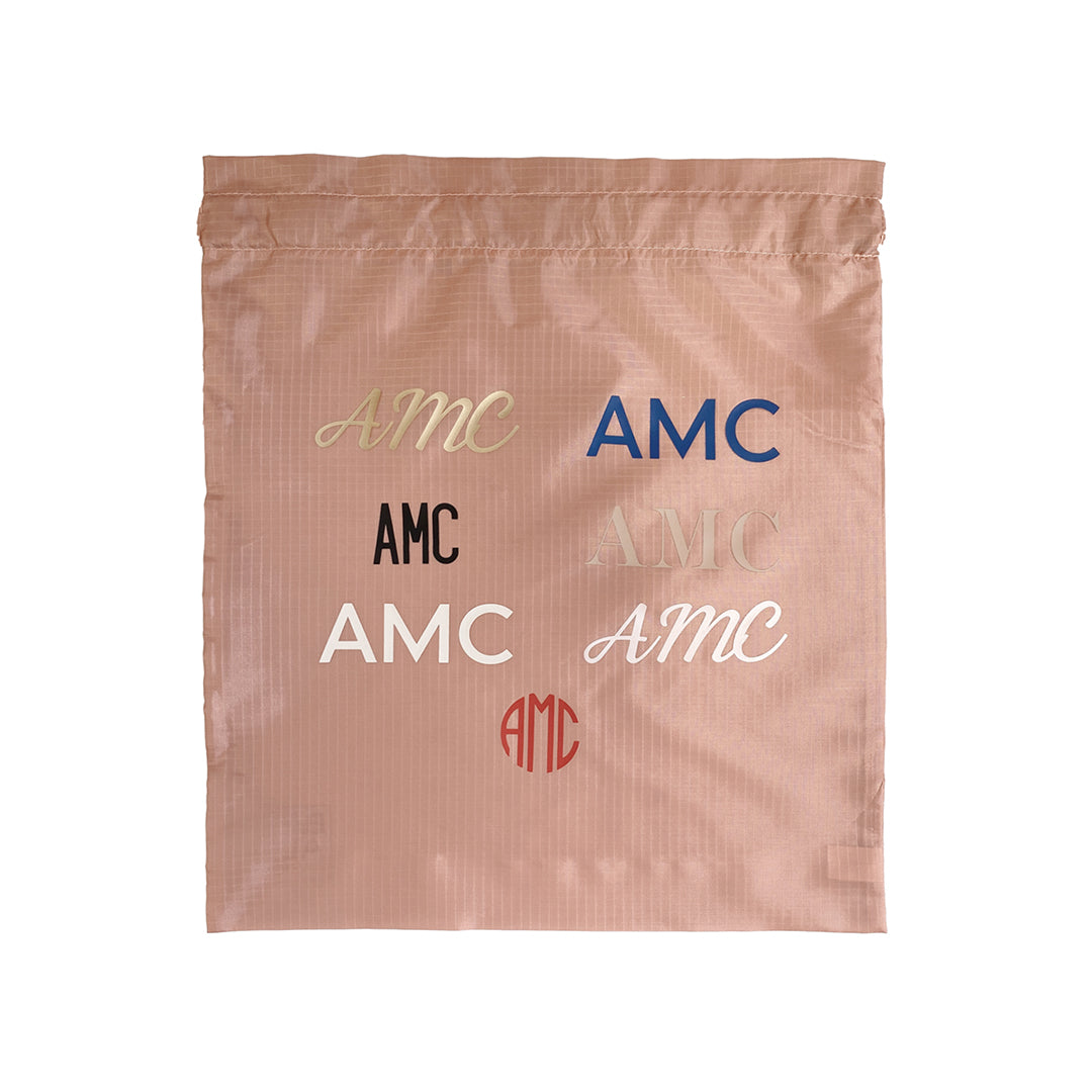 Bag-all Personalized Vinyl Bag showing different monogram styles and fonts in various colors including gold, blue, black, and red on a soft pink recycled nylon background