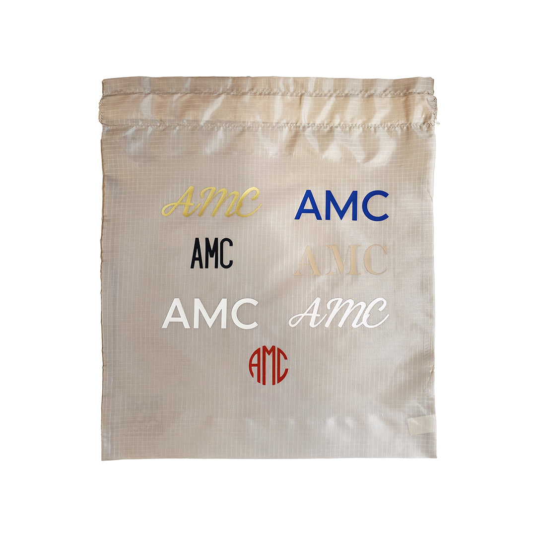 Bag-all Personalized Vinyl Bag showcasing various monogram styles in multiple colors including gold, blue, black, white, and red on a beige recycled nylon fabric background