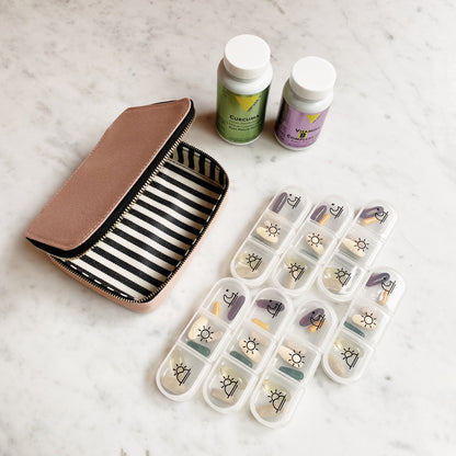 Bag-all Large Pill Travel Case in pink/blush with striped interior, featuring daily pill organizer compartments and zipper closure, displayed with supplement bottles on marble surface