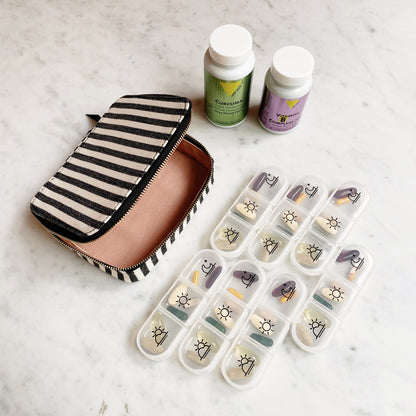 Bag-all Large Pill Travel Case with striped cotton design, daily organizer compartments, and zippered closure, shown with medicine bottles and pill containers on marble surface