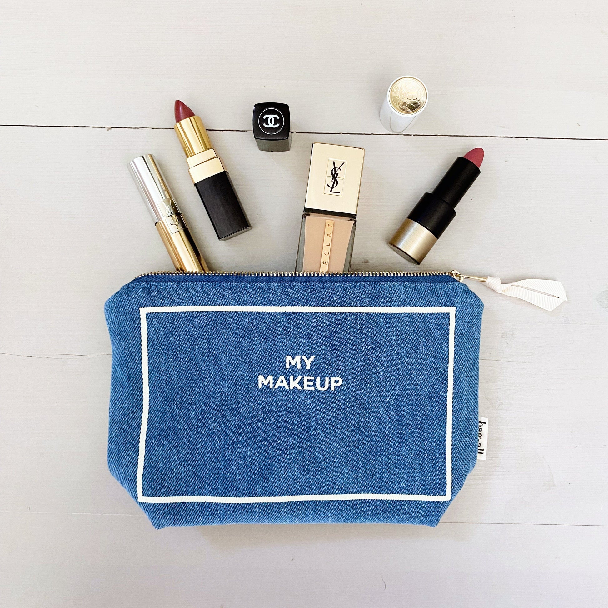 Bag-all My Makeup Pouch in denim with waterproof lining, displayed with luxury cosmetics including lipsticks and foundation, perfect for organizing daily beauty essentials