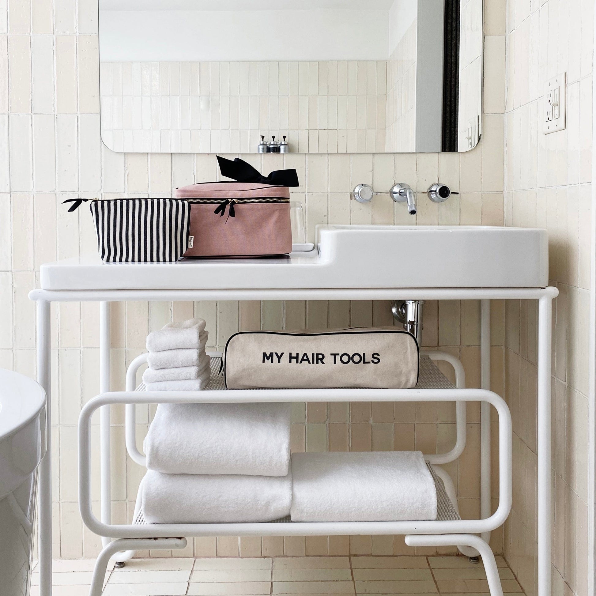 Bag-all Striped Makeup Pouch with pink waterproof lining displayed on white bathroom vanity shelf, alongside hair tools case and folded white towels, showcasing modern bathroom organization