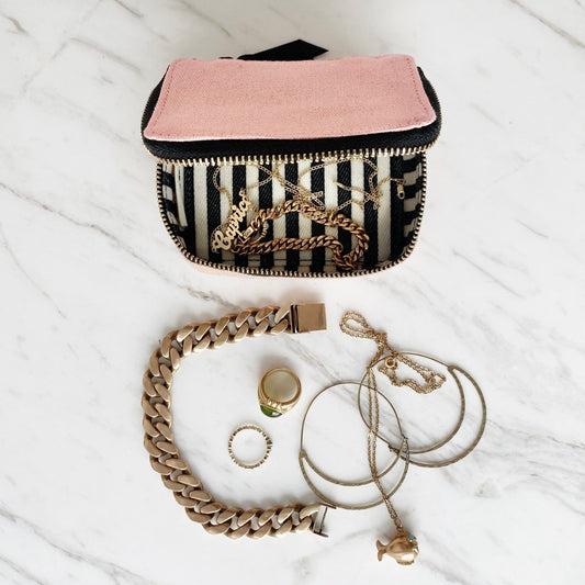 Bag-all Pink Jewelry Box with striped lining and gold zipper, shown with gold jewelry pieces including rings, chain bracelet and necklace on marble surface