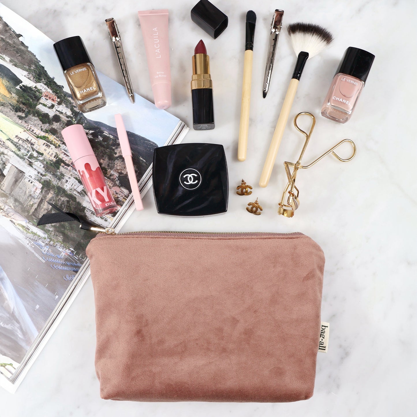 Bag-all My Makeup Pouch in pink velvet with waterproof lining, displayed with luxury cosmetics including makeup brushes, lipstick, and nail polish. Organized beauty essentials showcase pouch functionality.