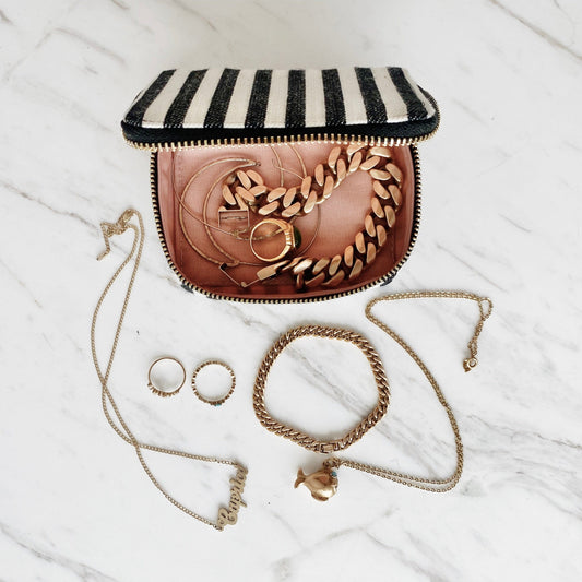 Bag-all Striped Jewelry Box with gold zipper displayed with elegant gold chain jewelry and rings on white marble background, showcasing portable storage solution