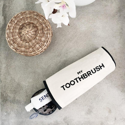 Bag-all cream toothbrush travel case with "My Toothbrush" text shown next to woven coaster and white orchids on concrete surface, minimalist Scandinavian design