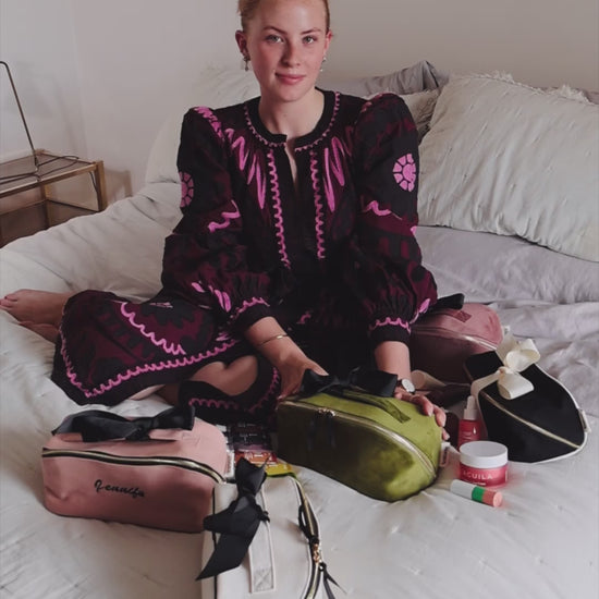 Woman sitting on a bed with Bag-all makeup and toiletry organizers, including the Accordion Box in Green Velvet. Stylish and practical beauty storage