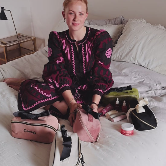 Woman sitting on a bed with Bag-all makeup and toiletry organizers, including the Accordion Box in Pink/Blush. Stylish and practical beauty storage