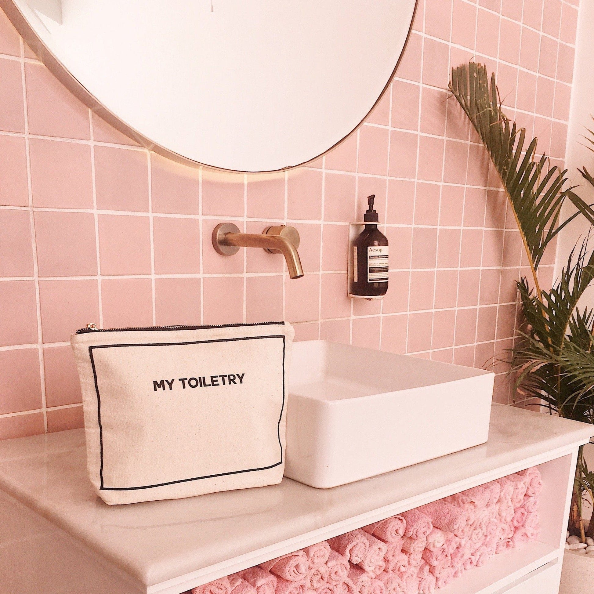 Bag-all Weekend Essential Packing Set 4-Pack in Cream featuring My Toiletry pouch displayed in modern pink bathroom with brass fixtures and minimalist white vessel sink