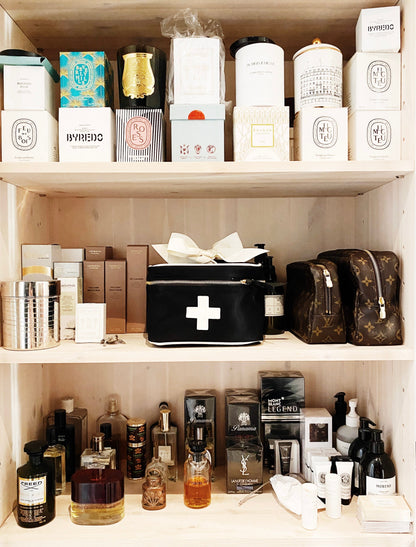 Bag-all Meds and First Aid Storage Box in black with white medical cross design, displayed on shelf with luxury items. Features metal zippers and carrying handle for organized storage.