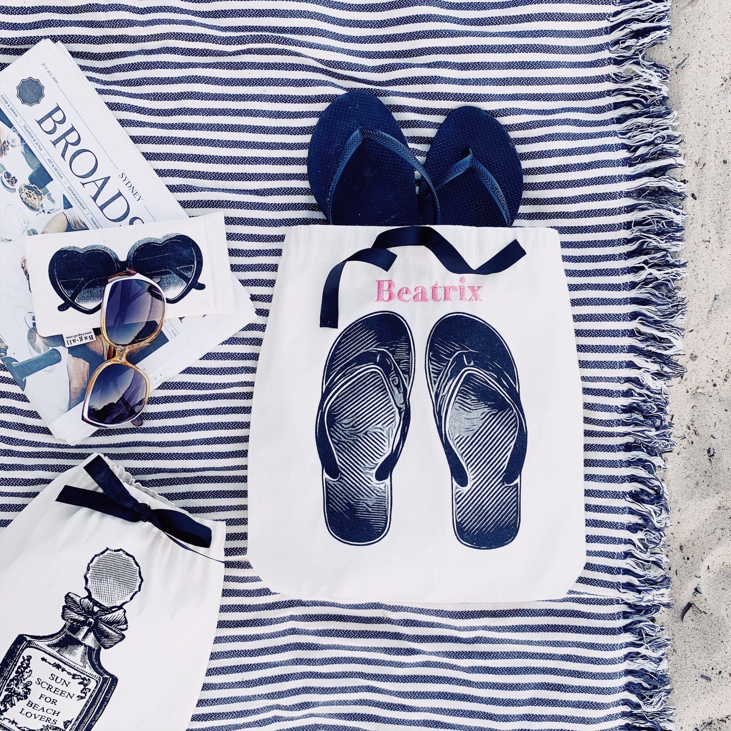 A striped beach towel with the flip flop shoe bag at the beach. 