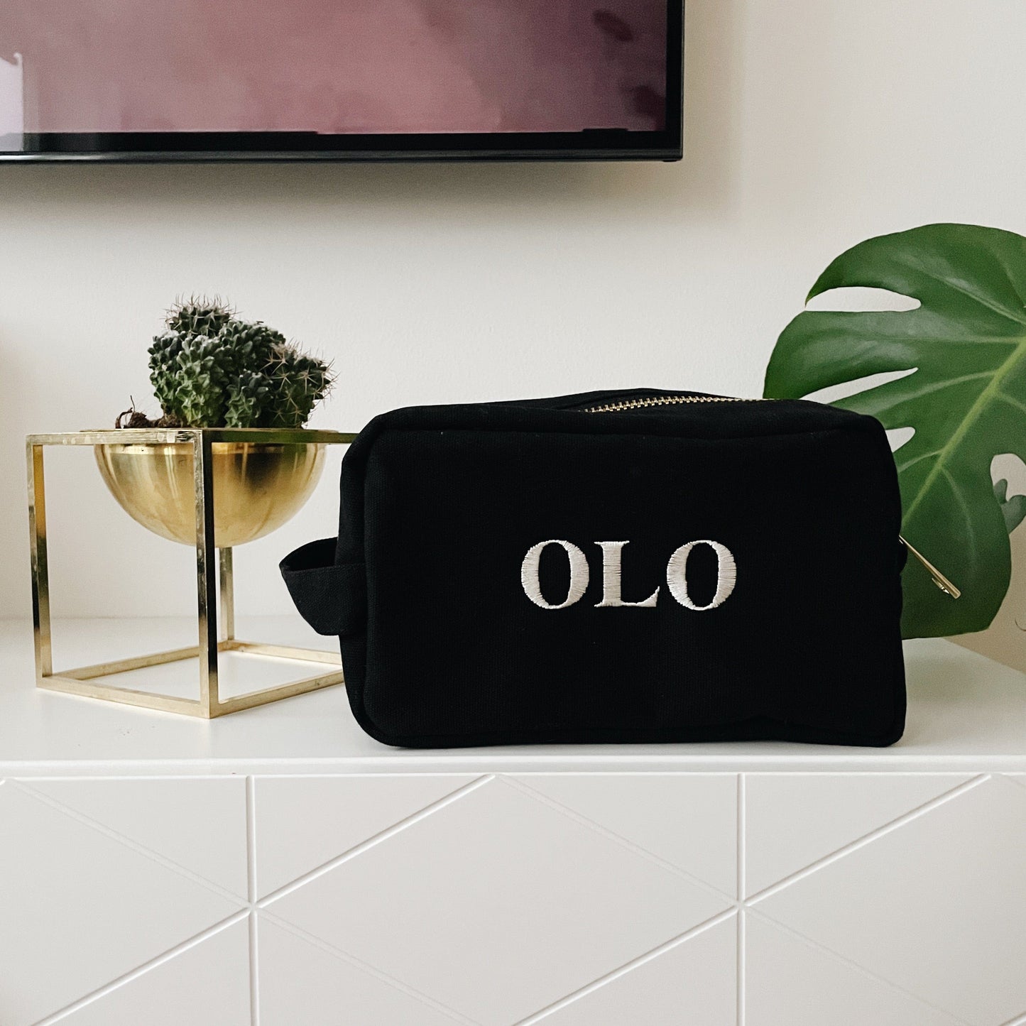 Bag-all Large Black Toiletry Bag with OLO monogram, elegant organizing pouch displayed on white shelf with gold planter and monstera leaf decor