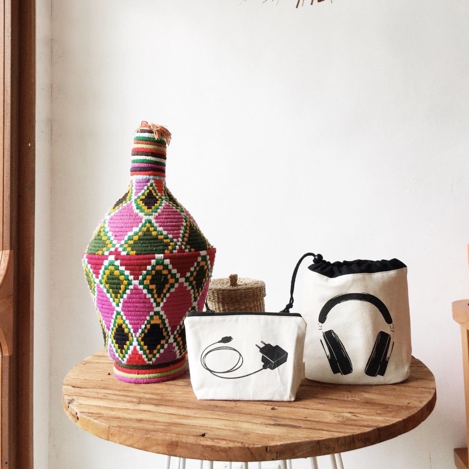 A wooden side table with decor, headphones case and a charger pouch. 