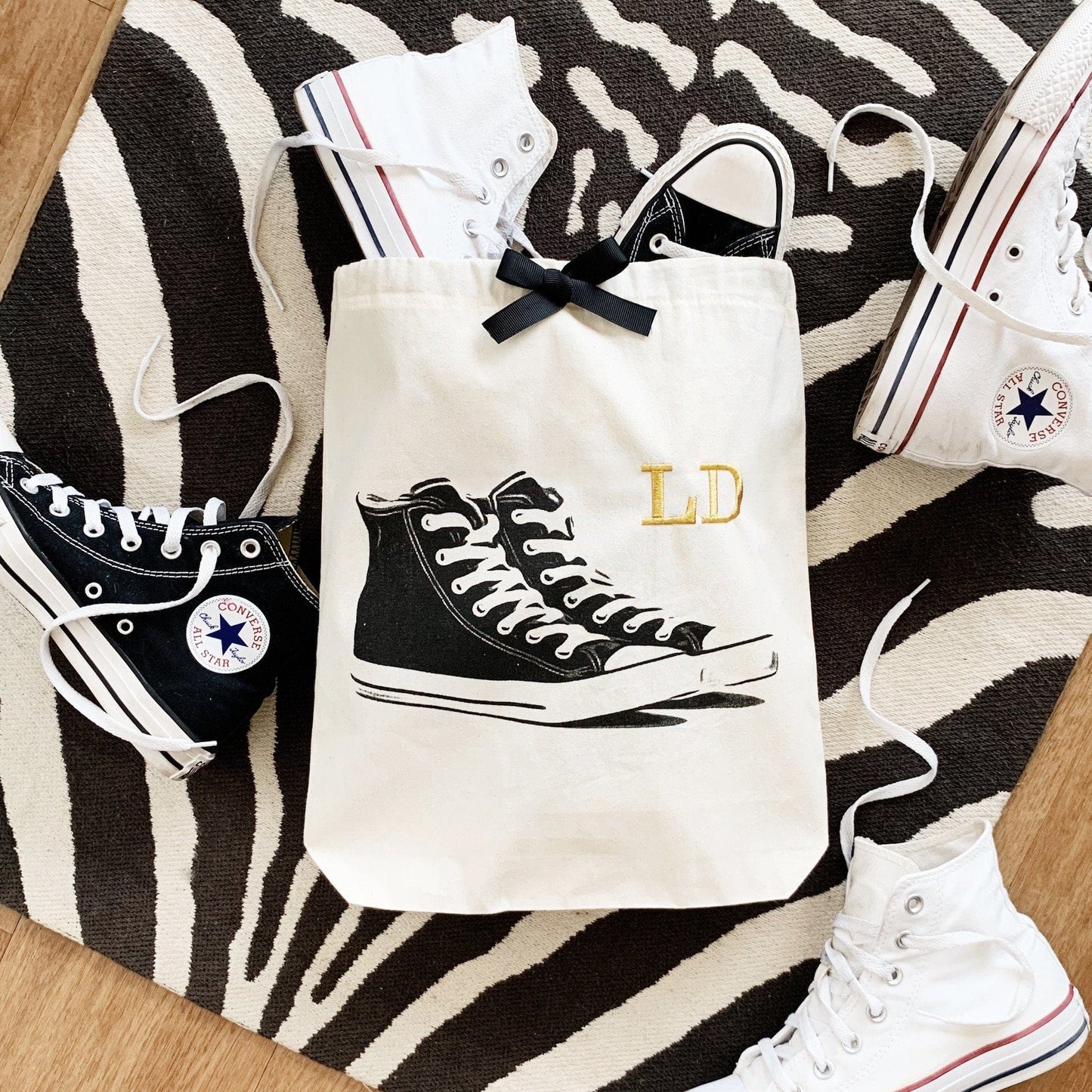 Bag-all Cream Sneakers Shoe Bag featuring black high-top sneaker print and gold monogram initials, displayed on zebra-pattern background with matching shoes, perfect for organized storage